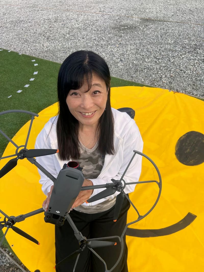 フィールドでドローンを手に笑顔を見せるチーフインストラクターの番場摩美